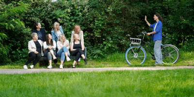 frauen-in-fuehrungspositionen_female-leadership_begleitung Frauen in Führungspositionen, Female Leadership, Frauengruppe auf Bank und Frau mit Fahrrad kommt hinzu